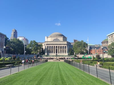 View of the Columbia University campus with green lawns and historic buildings under a blue sky.