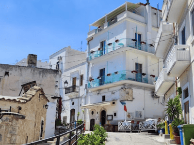 Ruelle pittoresque de Mattinata avec des maisons blanches, des balcons en fer et une végétation accueillante.