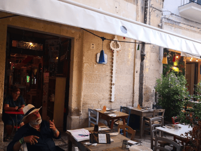 Terrasse de restaurant à D, avec des tables en bois, menus exposés et des décorations murales attirantes.