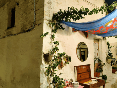 White wall covered with climbing plants, a wooden table with dishes, and a colorful cloth in Ceglie Messapica.