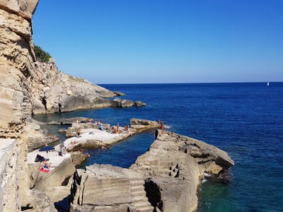 Rocky coast in Santa Cesarea Terme, with bathers enjoying the sun in crystal-clear water.
