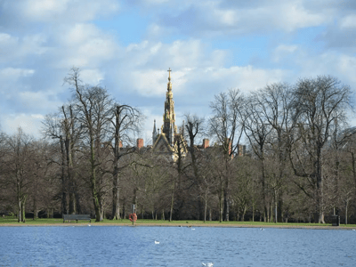 Peaceful view of Hyde Park, with the majestic architecture of the Royal Albert Hall behind a calm lake and trees.