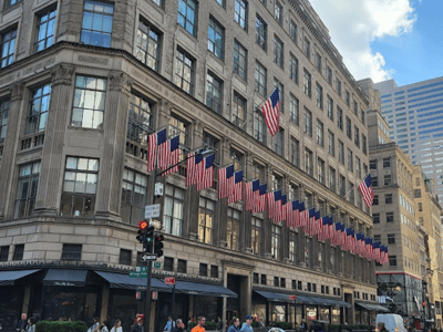 Historic façade with American flags on Fifth Avenue, bustling with pedestrians and cars.