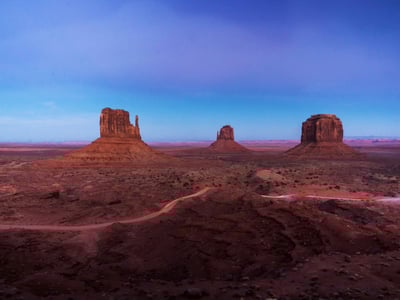 Vast panorama of Monument Valley, with its iconic rock formations under a violet sky at sunset.