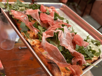 Pizza topped with arugula and ham, served at Adrienne's Pizzabar, an irresistible delight to savor.
