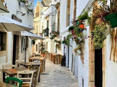 Lively street in Locorotondo, adorned with flowers and café tables, showcasing the picturesque charm of the Apulia region.