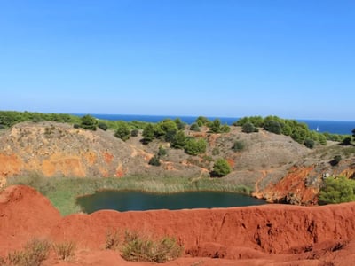 Lac de Bauxite, entouré de roches rouges et de verdure, sous un ciel bleu, offre un cadre naturel unique en Provence.