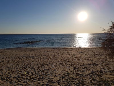 Coucher de soleil sur la plage de La Casa di Nico, illuminant les eaux calmes et le sable doré.