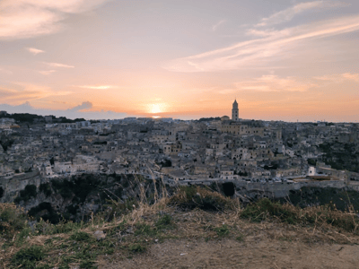 Vue panoramique de Matera au coucher du soleil depuis Belvedere Murgia Timone, mettant en valeur l'architecture historique de la ville.