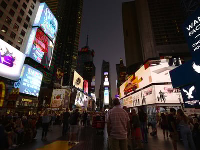Rues animées de Times Square, illuminées par des affiches publicitaires lumineuses, créant une atmosphère vibrante en soirée.