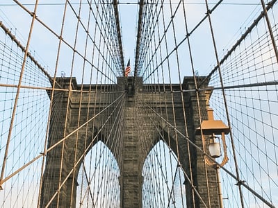 Suspension cables and majestic arches of the Brooklyn Bridge under a clear sky, showcasing the iconic architecture of New York.