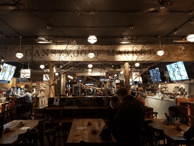 Atmosphère animée du Gansevoort Market à New York, avec des tables en bois et des stands de nourriture variée.