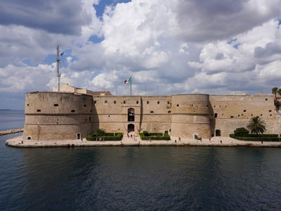 Aragonese Castle by the water, surrounded by impressive clouds and the Italian flag fluttering in the wind.