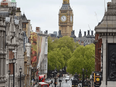 View of Big Ben, surrounded by lush trees and a bustling street in London, symbolizing British architecture.