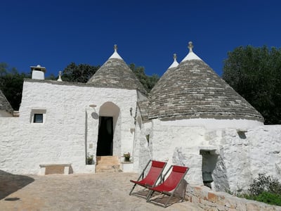Maison traditionnelle de style trullo à Borgo Canonica, avec chaises longues rouges sous un ciel clair.