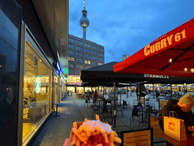 A portion of currywurst and fries, with the Berlin television tower in the background at Curry 61.