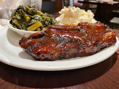 Juicy barbecue ribs served with green vegetables and mashed potatoes, typical of Sylvia's cuisine in Harlem.