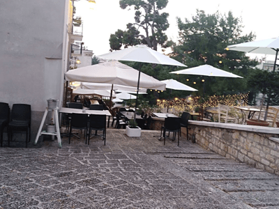 Terrasse animée du Restaurant Il Giullare, équipée de parasols blancs, parfaite pour un dîner en plein air.