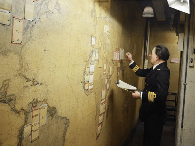 Officier en uniforme examinant une carte du monde aux Churchill War Rooms, marquant des stratégies militaires pendant la Seconde Guerre mondiale.