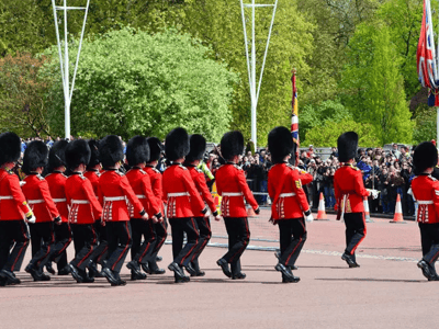 British guards in red uniforms march in front of Buckingham Palace, attracting an awestruck crowd.