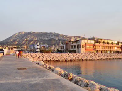 Port of Dénia at dusk, featuring moored boats and colorful houses reflecting a Mediterranean atmosphere.