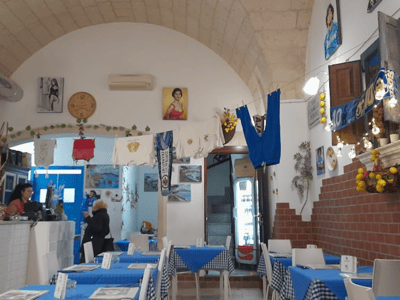 Intérieur chaleureux de Pizzeria Malafemmena, avec des tables à carreaux bleus et des œuvres d'art murales. Ambiance conviviale.