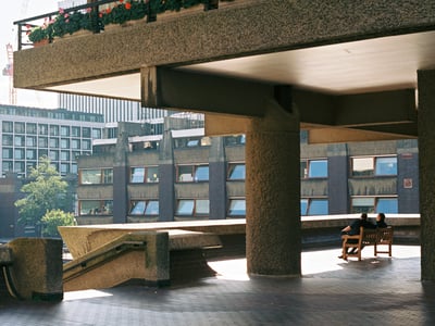 Espace architectural du Barbican, montrant des structures de béton et un banc surplombant les fenêtres modernes.