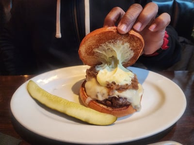 Un burger juteux du Five Napkin Burger, garni de fromage fondu et servi avec une tranche de cornichon.
