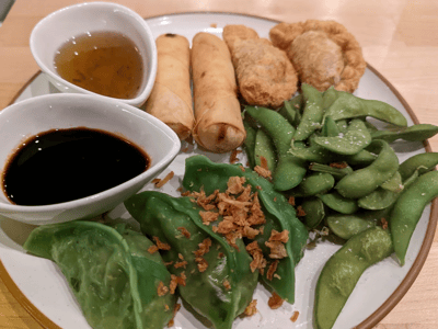 Assortiment d’entrées vietnamiennes à Plum Restaurant : rouleaux de printemps, edamame et raviolis verts, accompagnés de sauces.