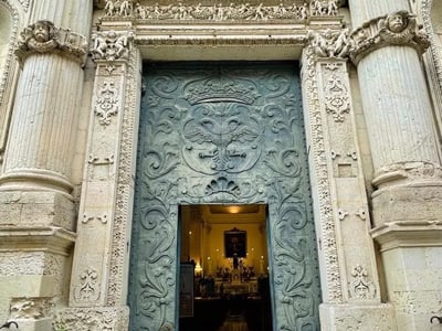 Entrée ornée d'une porte sculptée, à Lecce, reflétant l'architecture baroque et l'histoire locale.