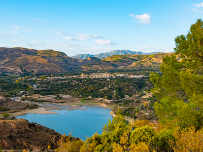 Vue panoramique de Melegís, illustrant un paysage montagneux et un lac paisible entouré de verdure.