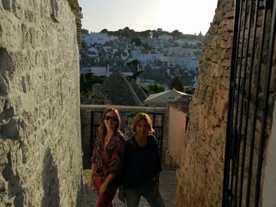 In the Aia Piccola district, two women pose at twilight, surrounded by traditional trulli architecture.