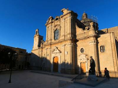 Baroque church in Oria, with an ornate facade, a clear blue sky, and a statue in the foreground, symbol of the local heritage.
