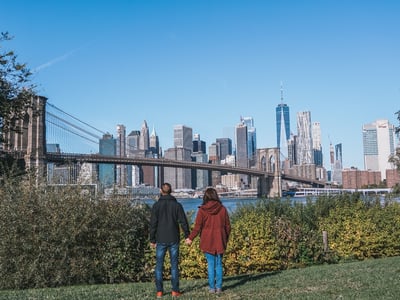 Couple admiring the New York skyline from Dumbo, with the Brooklyn Bridge and modern buildings in the background.
