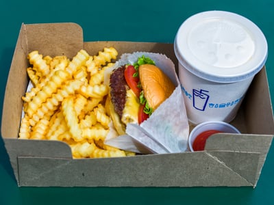 Un burger juteux avec fromage, salade et tomate, servi avec des frites ondulées et une boisson à Shake Shack, Théâtre District.