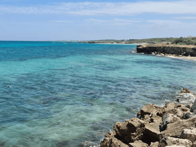 Panoramic view of the turquoise sea at Torre Specchia Ruggeri, with rocks and a sunny coast in the background.