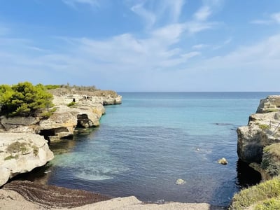 Panoramic view of the Caves of Poetry, showing coastal rocks and a turquoise sea under a clear sky.
