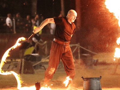 A man juggling with fire during the Palio d'Oria competition under spectacular lighting.