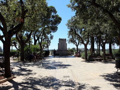 Sunny stroll in the Villa Comunale, surrounded by trees, with benches and a monument in the center. Perfect for relaxing.