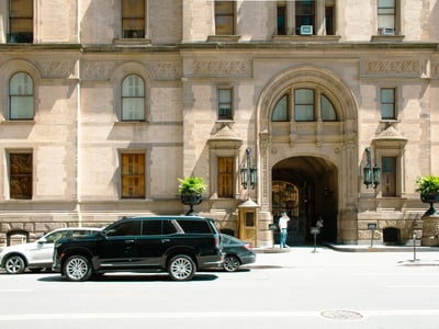 Entrée de la célèbre Dakota Building à New York, avec des voitures stationnées et des lanternes décoratives.