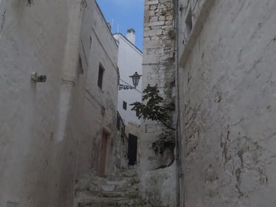 Narrow, cobbled street of Ostuni, with white stone walls and an antique lamp, evoking the picturesque charm of the city.