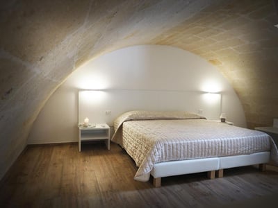 Chambre élégante à Albero della Vita, avec un lit confortable et un éclairage doux sous un plafond voûté en pierre.