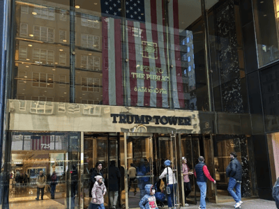 The entrance of Trump Tower in New York, with a large American flag and visitors exploring the famous structure.