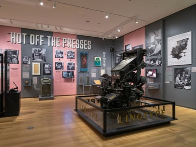 Exhibition on printing at the Museum of the City of New York, featuring a Linotype machine surrounded by historical photographs.