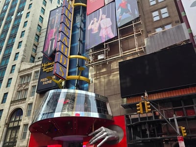 Entrée du musée de cire Madame Tussauds à New York, avec affiches de célébrités et une main en cire sortant du bâtiment.
