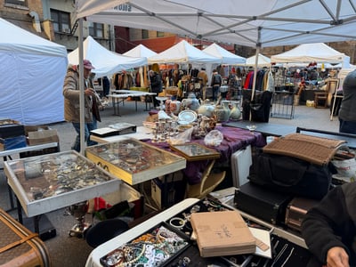 Marché aux puces de Chelsea, avec des stands de vêtements vintage et des objets anciens présentés sous des tentes blanches.