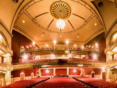 Interior view of the Apollo Theater, with red seats and a decorative ceiling, illuminated for a show.