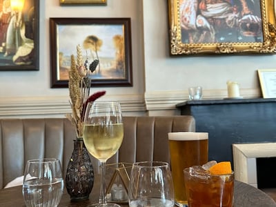Elegantly set glasses on a table at Prince Bonaparte, with cocktails and artwork on the wall.