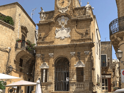 Historic building at Piazza Manfredi, showcasing baroque architecture and an ornate clocktower.