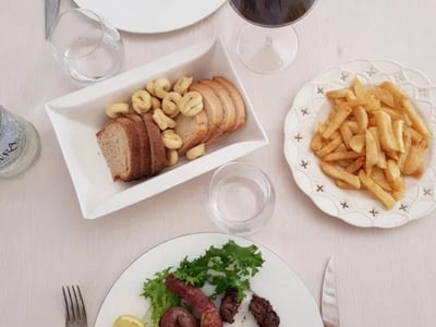 Repas copieux à la Taverna della Torre, incluant viande grillée, frites et pain, accompagné d'un verre de vin rouge.